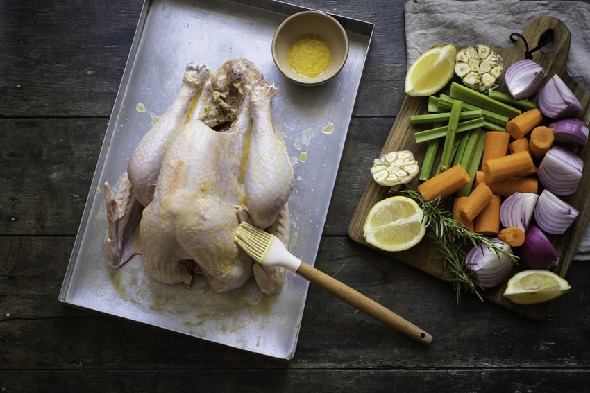 image shows a raw turkey being brushed with butter before being stuffed with vegetables