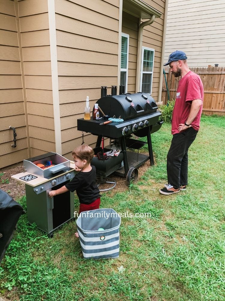 image shows a man using a smoker with a child using a toy grill next to him