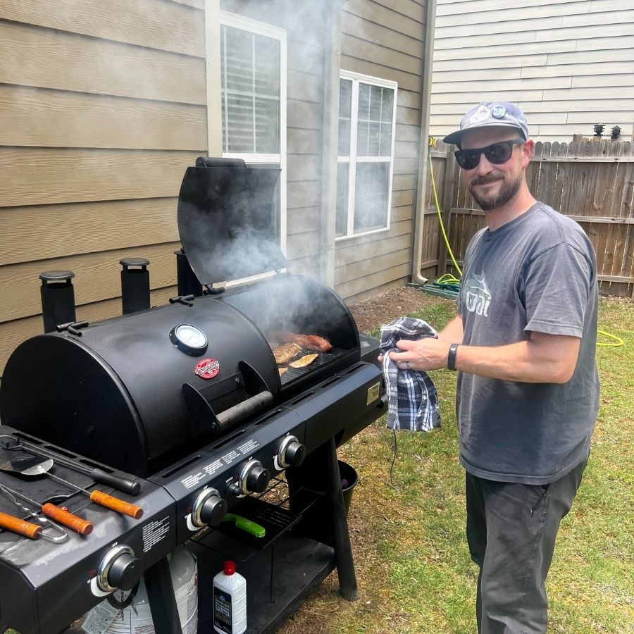 image shows a man standing at a backyard smoker