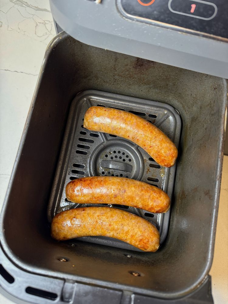 image shows cooked brats in an air fryer basket