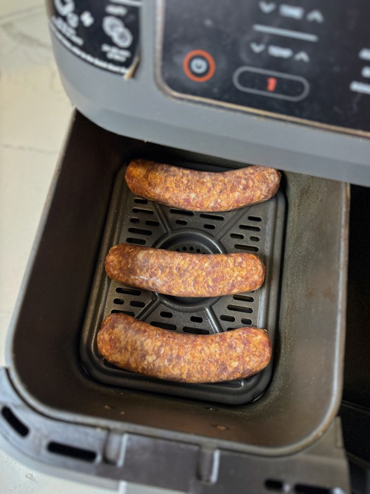 brats in an air fryer basket before cooking