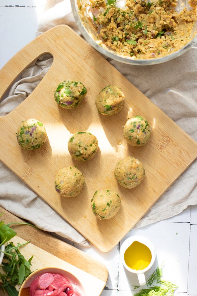 image shows uncooked falafel balls on a wood cutting board